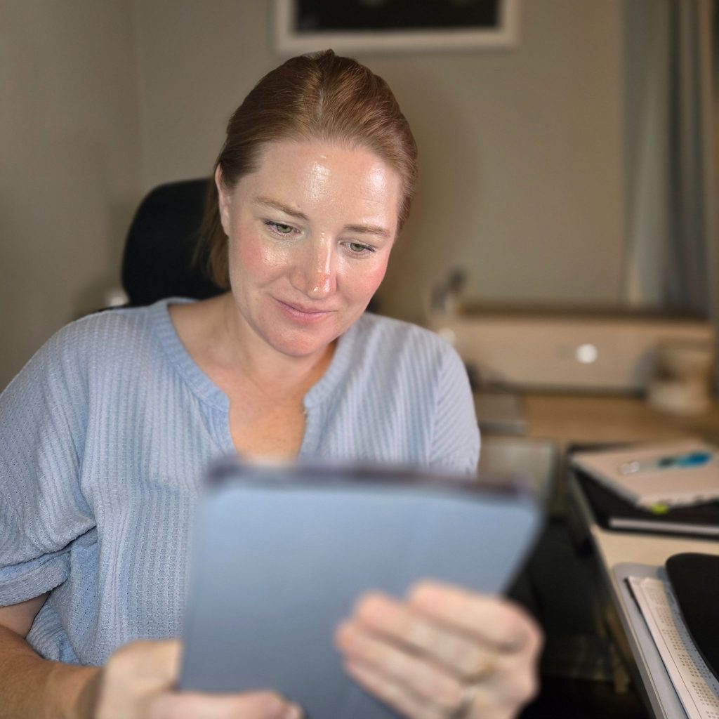Raena sitting at her desk holding her tablet with an admiring look on her face. 