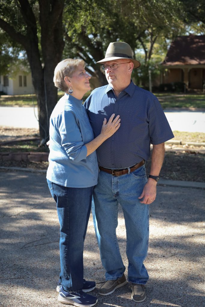 Older couple looking at each other and smiling while standing on a tree-lined path