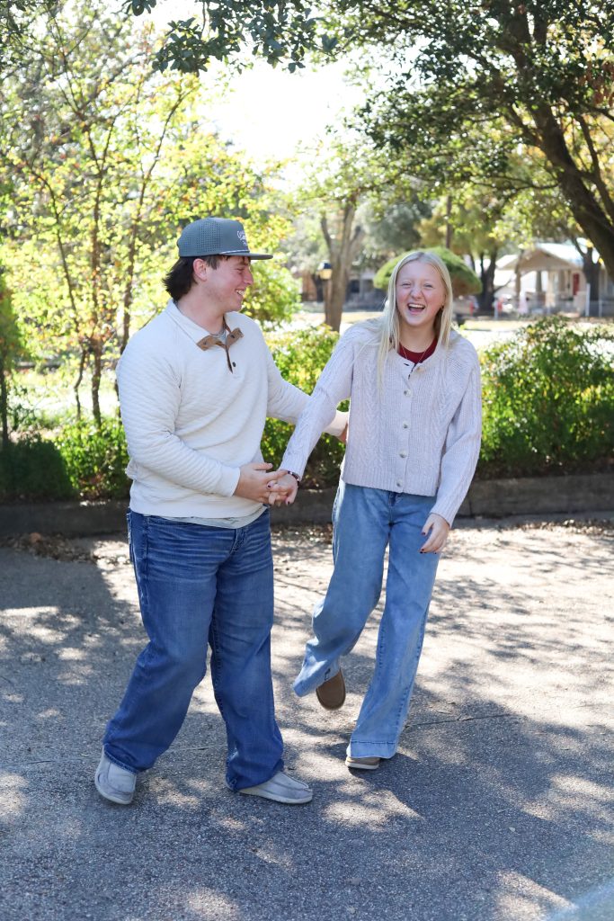 Young teen couple holding hands and laughing while walking outdoors in a fall setting