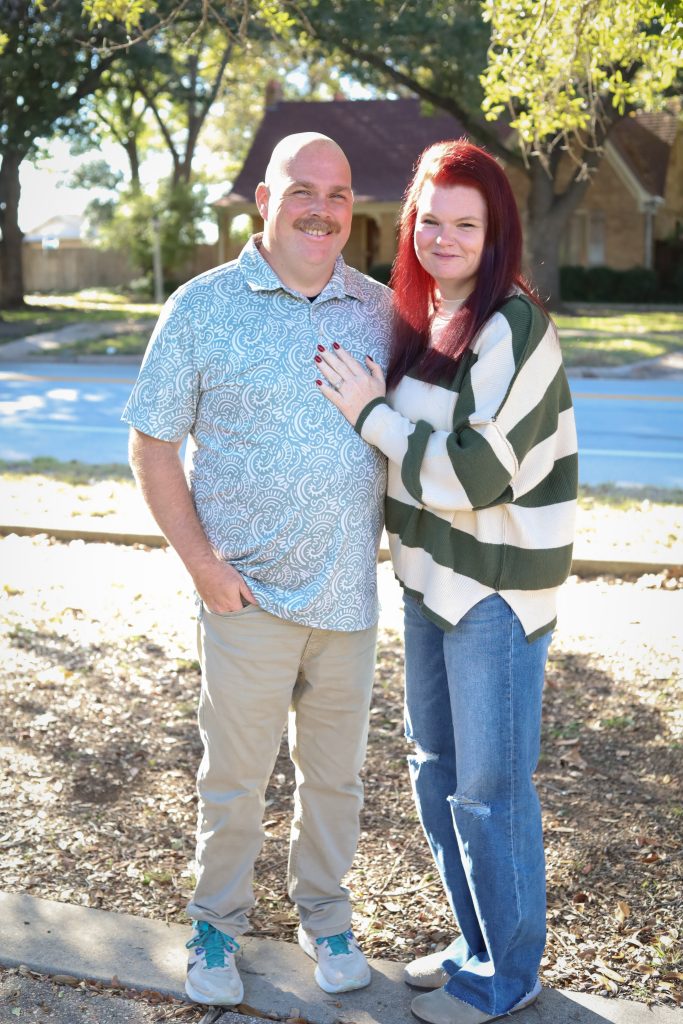 Young couple standing together outdoors on a residential street, smiling during a natural light portrait session
