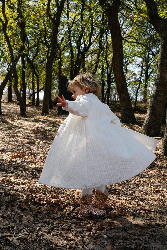 Young child wearing a dress twirling on a leaf-covered path in the woods